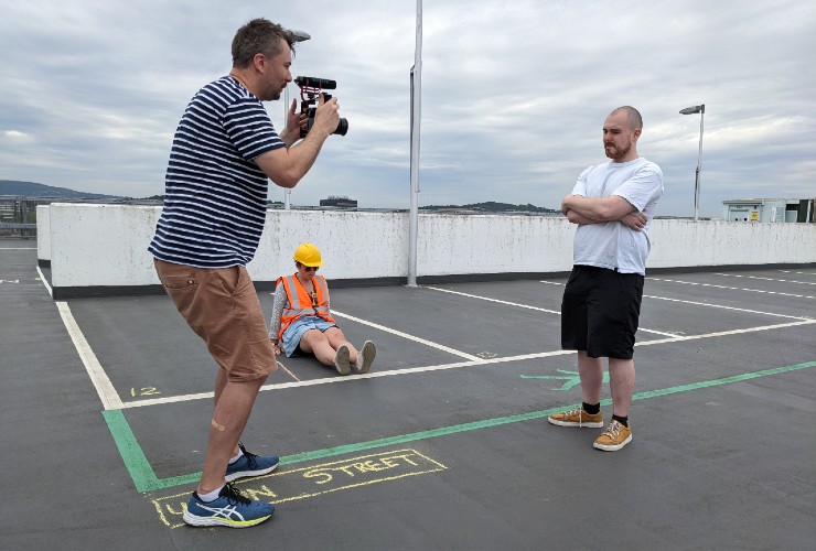 Man filming standing interview subject on empty blacktop parking lot