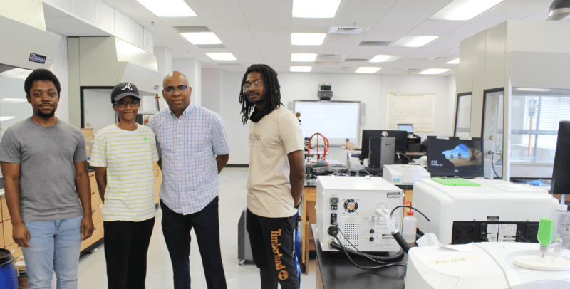 Four students stand in lab filled with electronic equipment