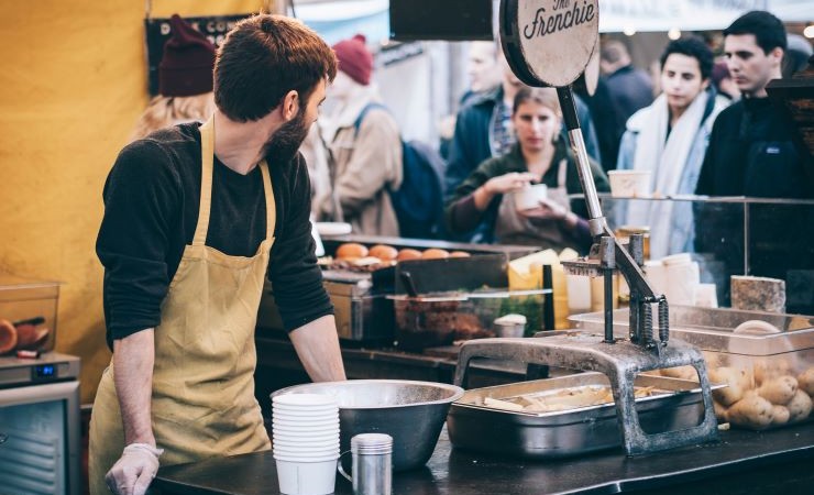 Photo of a cafe worker in a yellow apron leaning against the counter and looking back at some frowning customers.