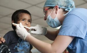 Dental technician in scrubs uses toothbrush on boy