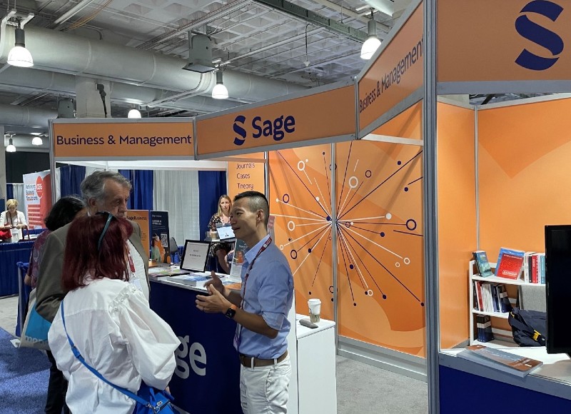 Man talks with man and women in front of Sage-branded exhibit booth