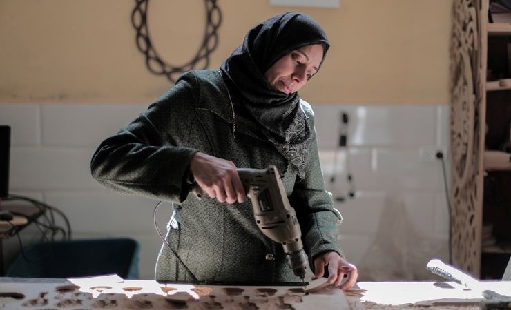 A hijabi factory worker assembles parts at a workstation.