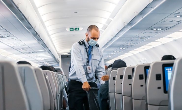 Image: Flight attendant in surgical mask collects trash from airline passengers.