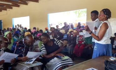 Man and woman standing at front of completely filled hall hold up papers