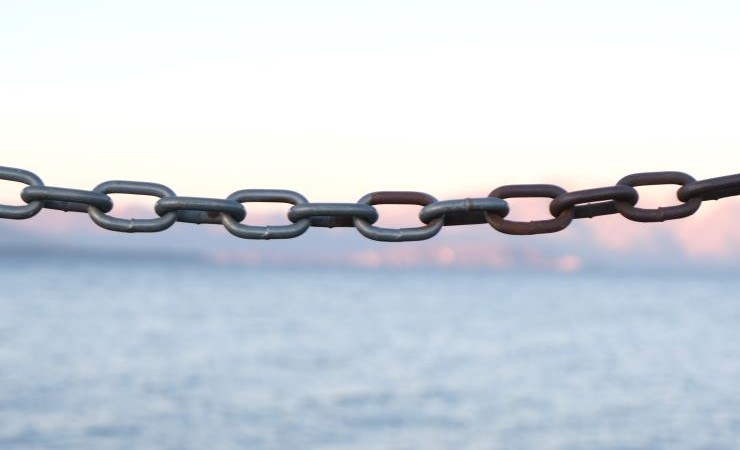 Close up photograph of a steel chain with a shoreline in the background.