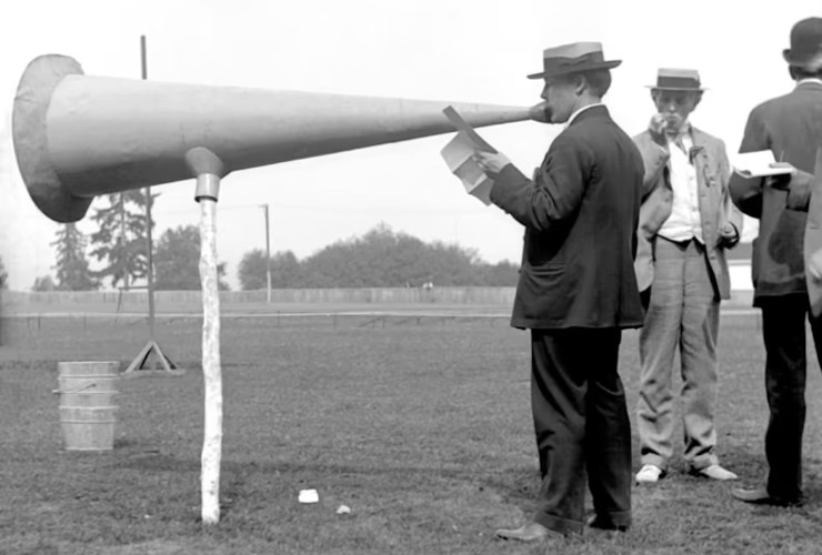 Black and white photo of man from circa 1900 speaking into giant megaphone on a stick