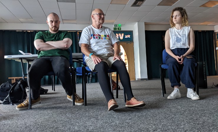 Three causally dressed people sitting on chairs in a row in an empty conference room