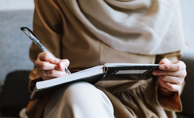 Close-up image of employee in hijab writing in notebook.