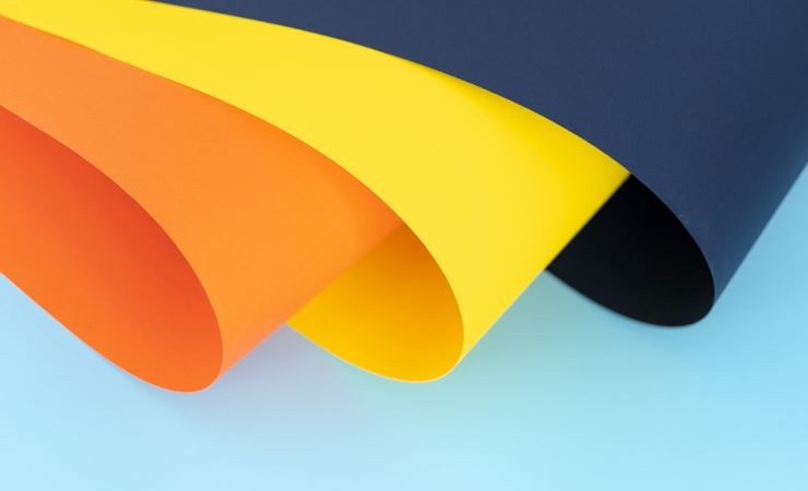 Abstract image of orange, yellow, and navy-blue paper on light blue background.