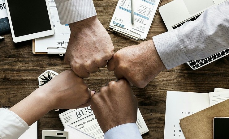 Four employees fist bump over workspace.