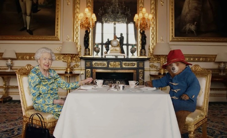 Scene from video showing Queen and paddington bear at table in ornate room