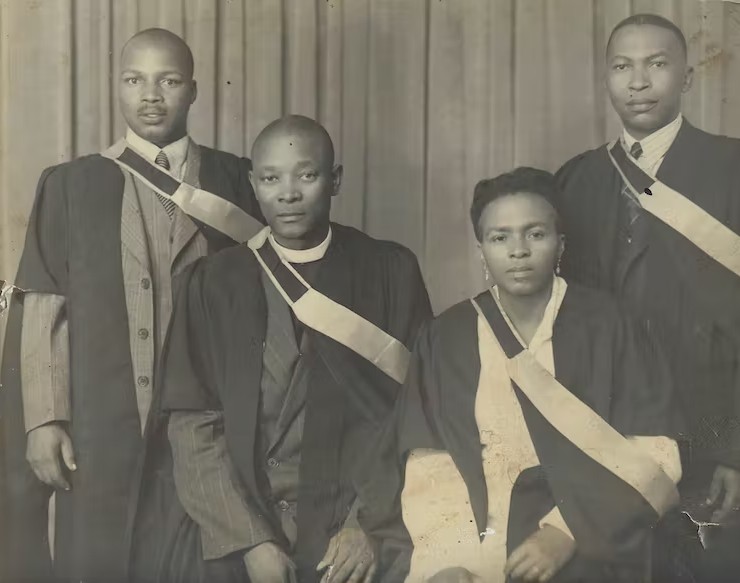 Four young adults in graduation robes, three male and one female in black and white photo