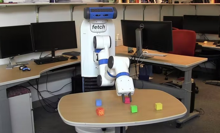 Human size device with one arm and two 'fingers' moves colored blocks on a table