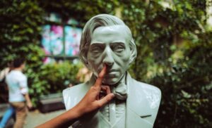 Close-up photograph of a bust and a real, human hand picking its nose.