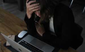 A woman at a laptop, appearing stressed.