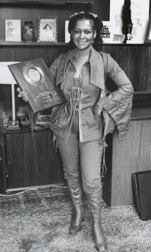 A smiling Sylvia Robinson holds a gold record plaque at her side