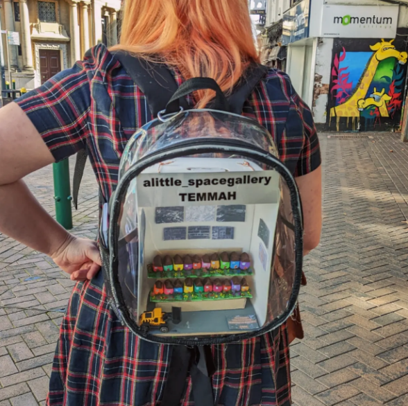Woman facing backwards, displaying a backpack with the title "alittle_spacegallery TEMMAH."