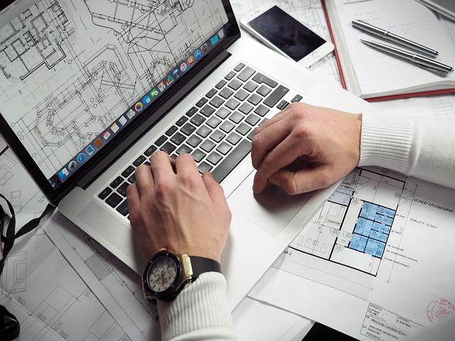 Hands sit on a laptop showing a blueprint.