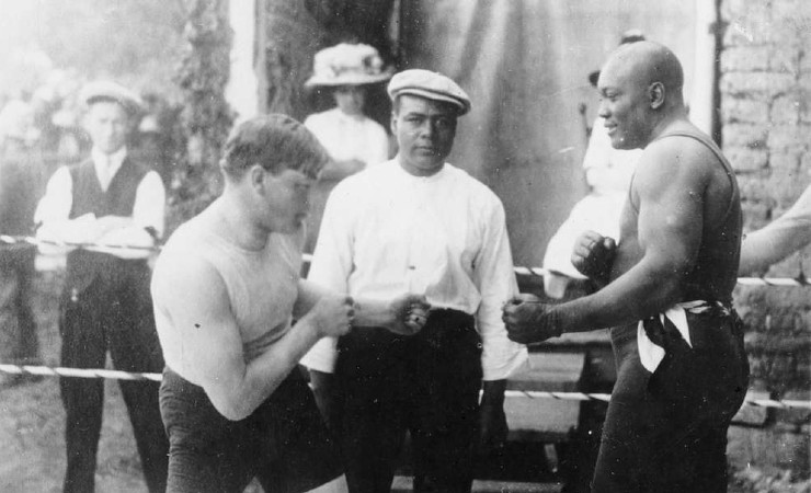 Black and white staged picture of two boxers in fighting stance with fists extended and referee in background.