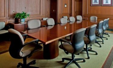 Empty seats surrounding large meeting table in wood-paneled room