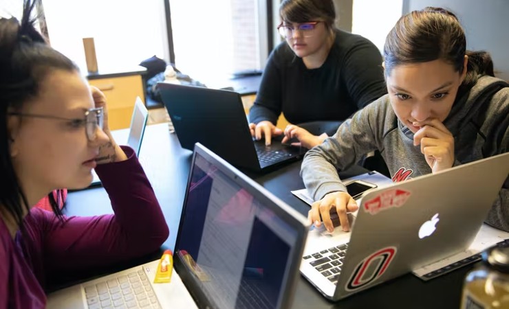 Three female students at table with laptops open collaborating