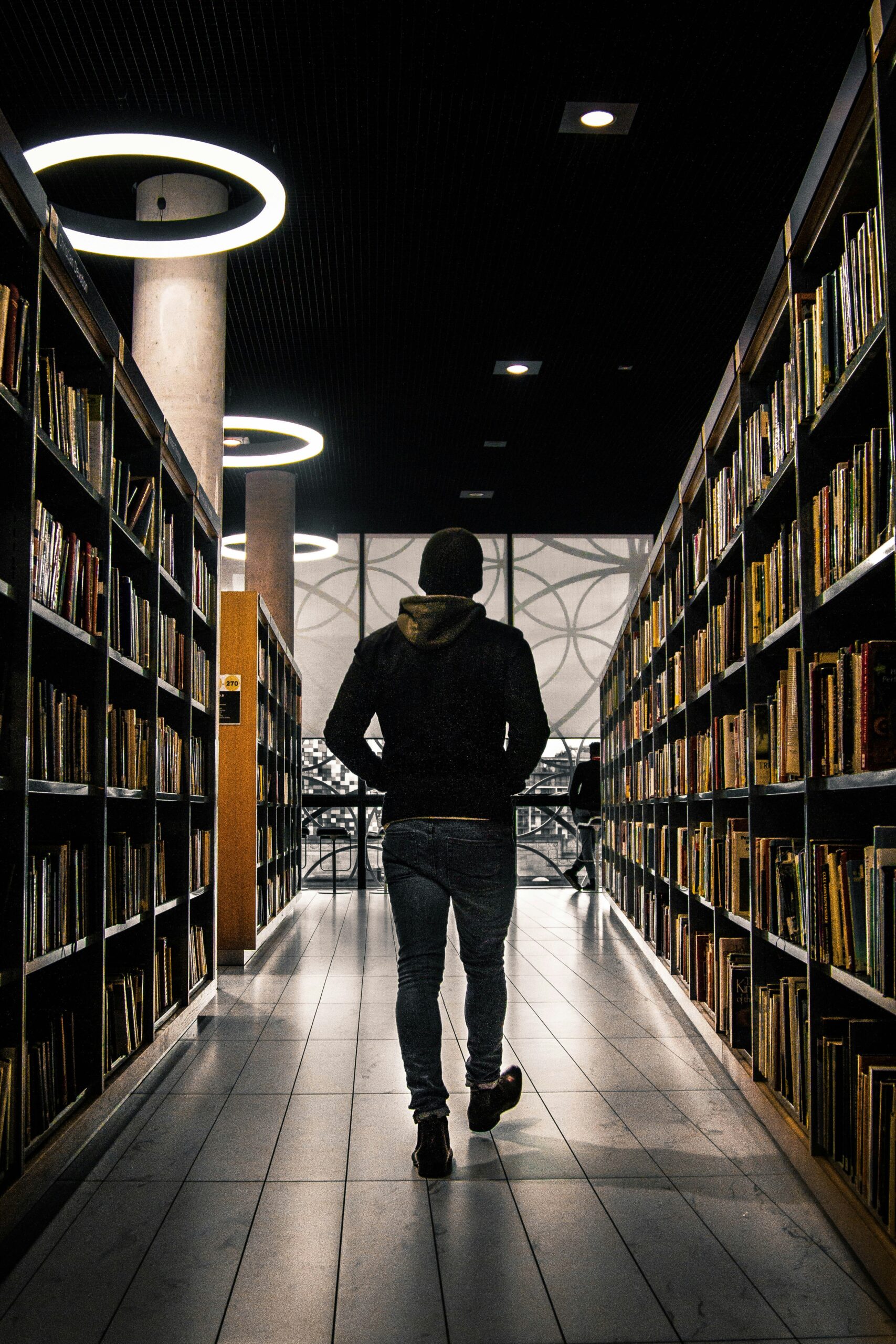 Silhouette of patron walking aisle on books in library