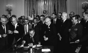 LBJ surrounded by men in suits as he signs bill