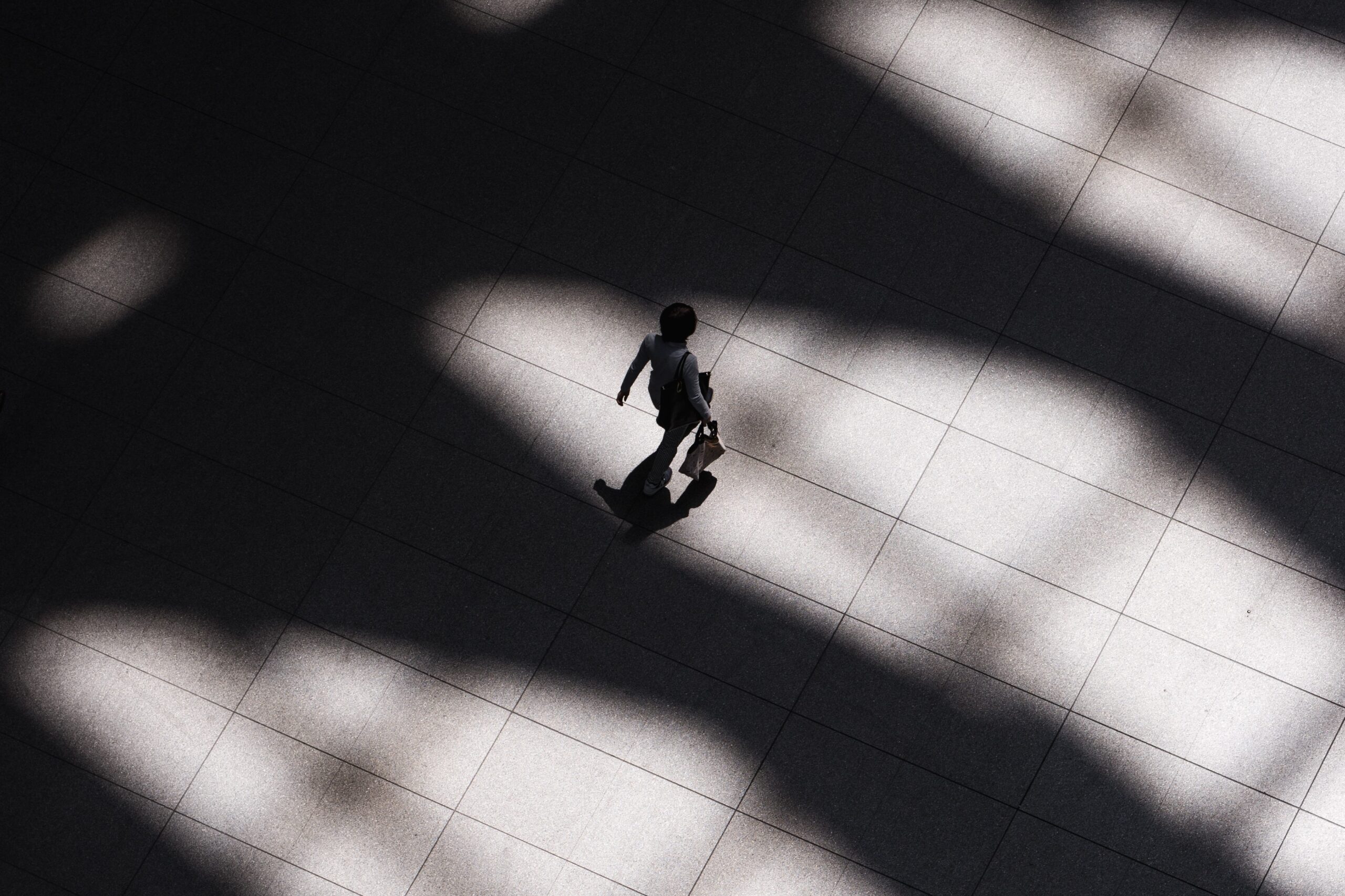 Aerial black and white view of a woman walking alone across a vast space