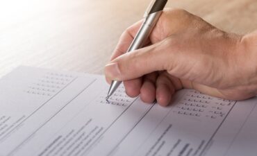 A person's hand fills out survey with pen.