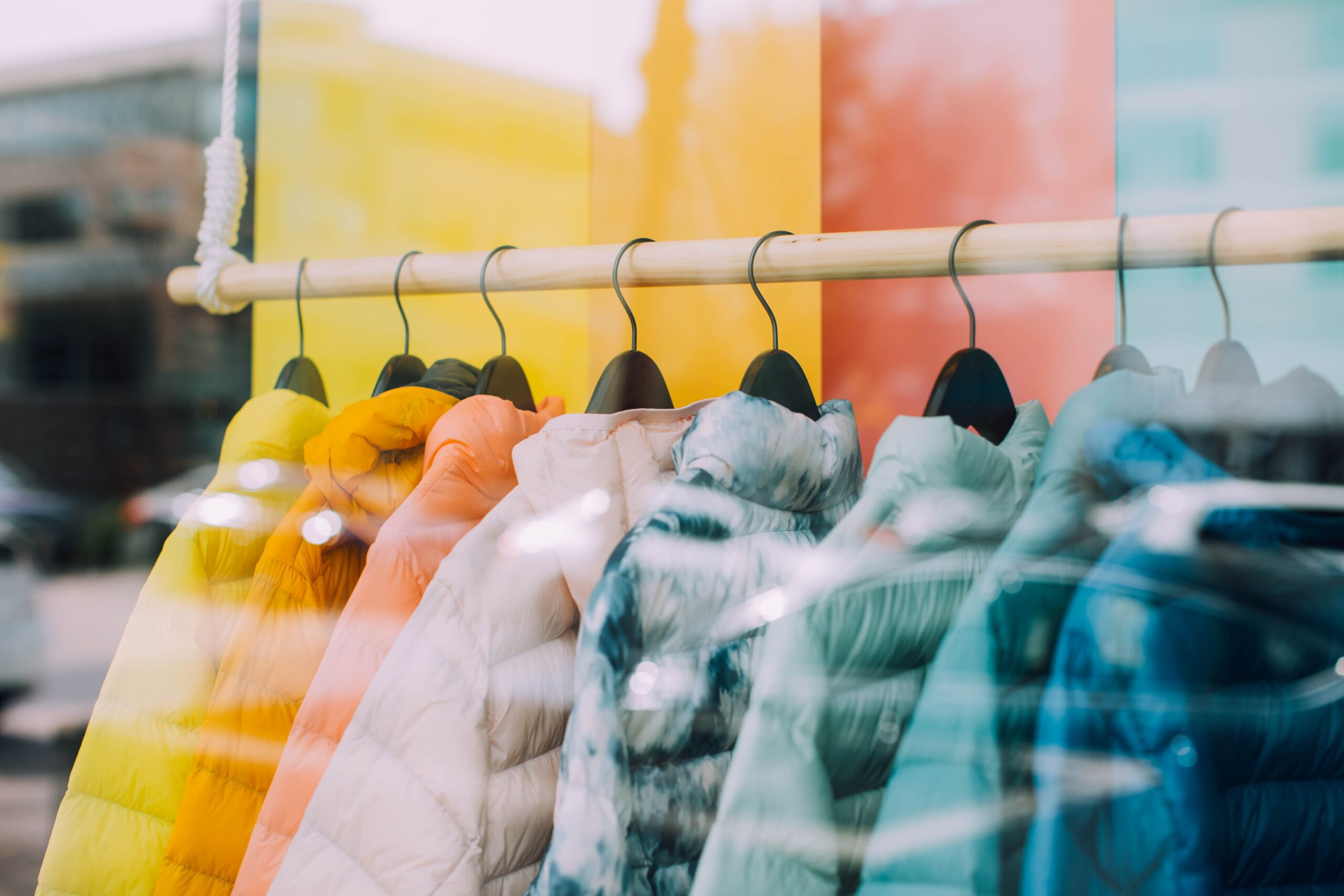 Colorful jackets pictured on rack in storefront.