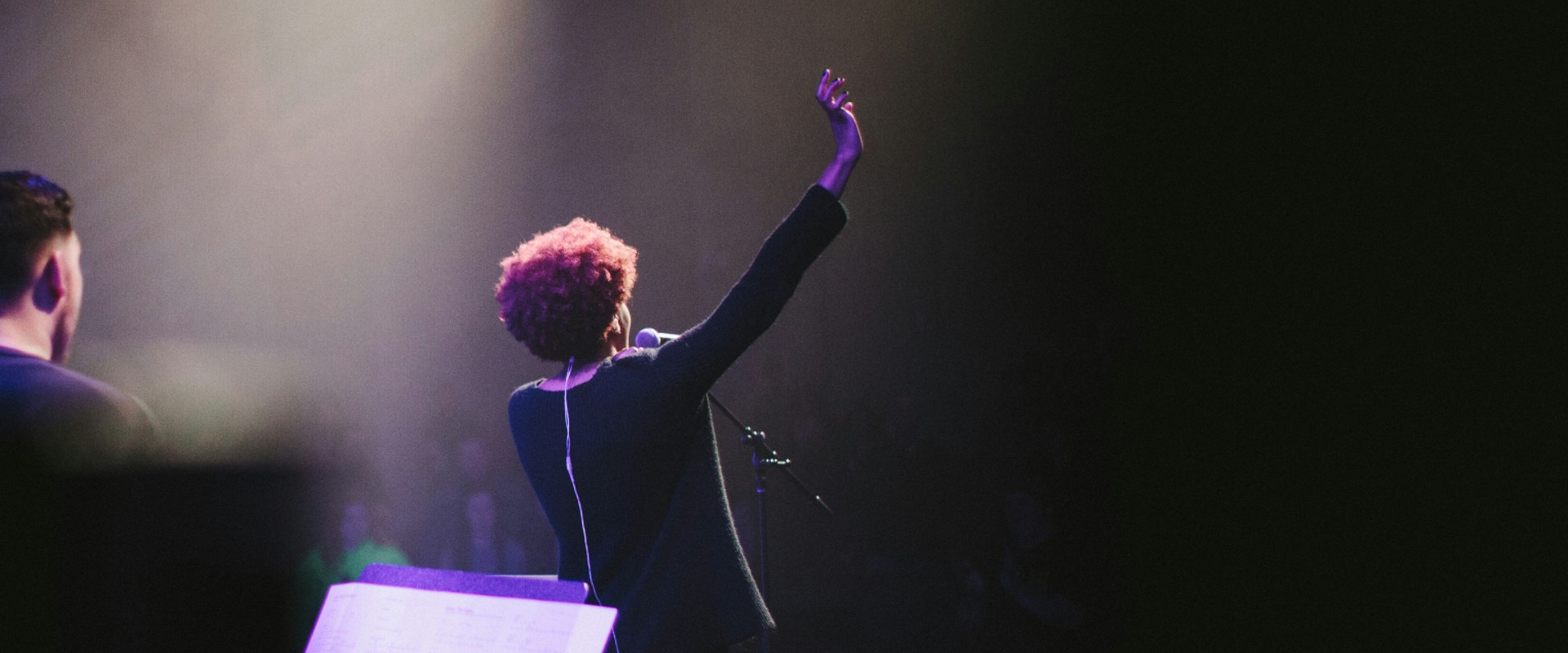 female singer with arms raised before audience seen from backstage